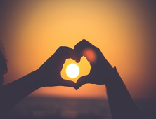 Silhouette of two hands forming a heart shape around the setting sun at sunset