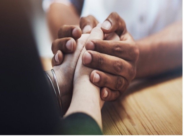 Two people holding hands in a gesture of support or comfort, with one person's hand resting on the other's.